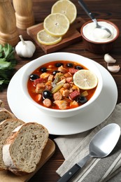 Photo of Meat solyanka soup with sausages, olives and vegetables served on wooden table