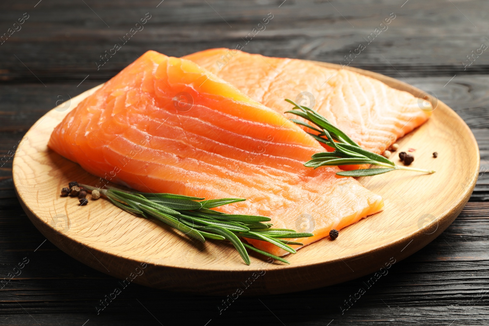 Photo of Wooden plate with tasty salmon fillet on black table, closeup