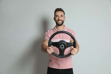 Happy man with steering wheel on grey background