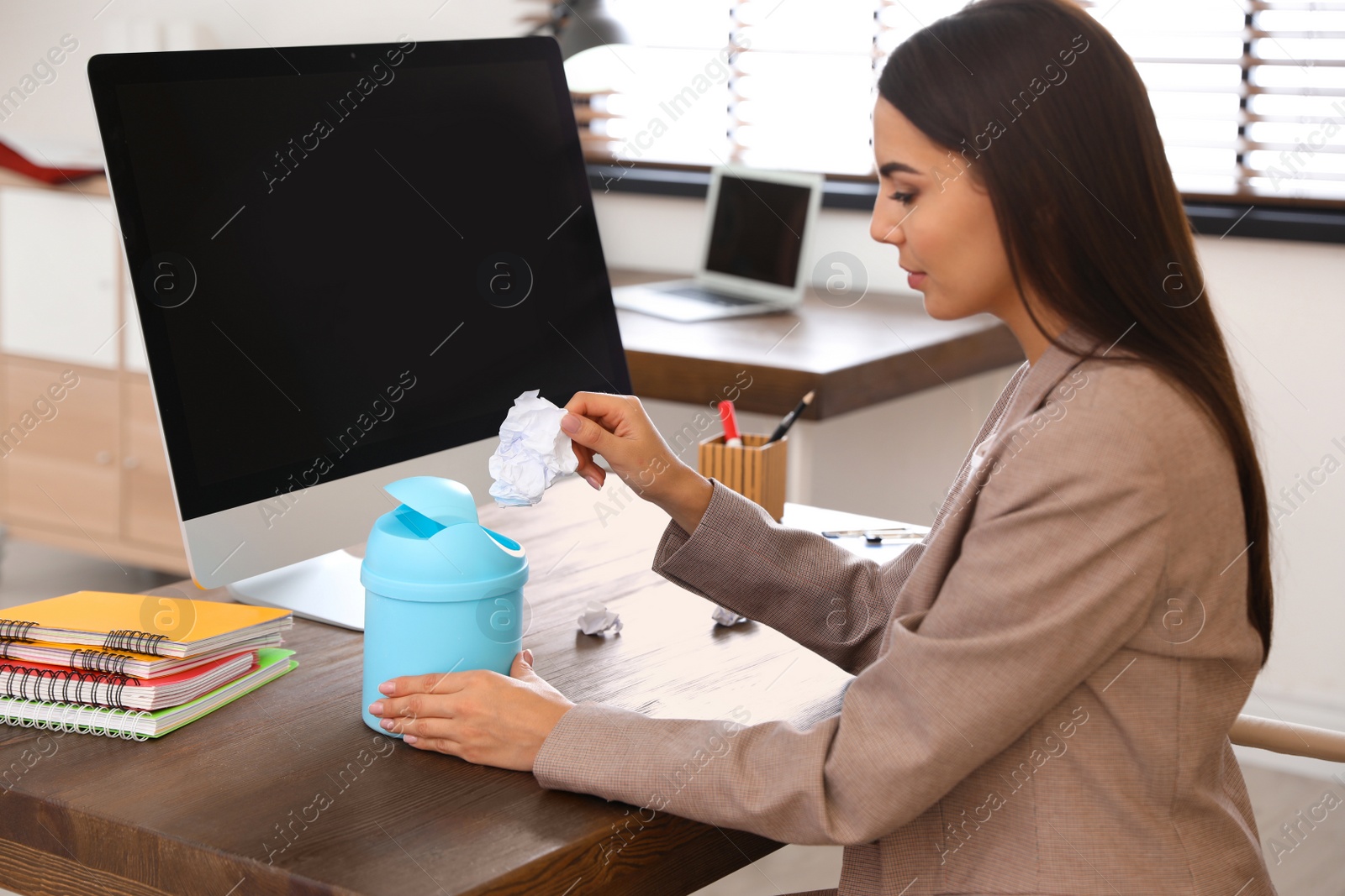 Photo of Young woman throwing paper into recycling bin at office