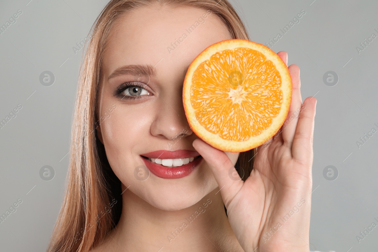 Photo of Young woman with cut orange on grey background. Vitamin rich food