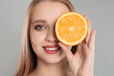 Young woman with cut orange on grey background. Vitamin rich food