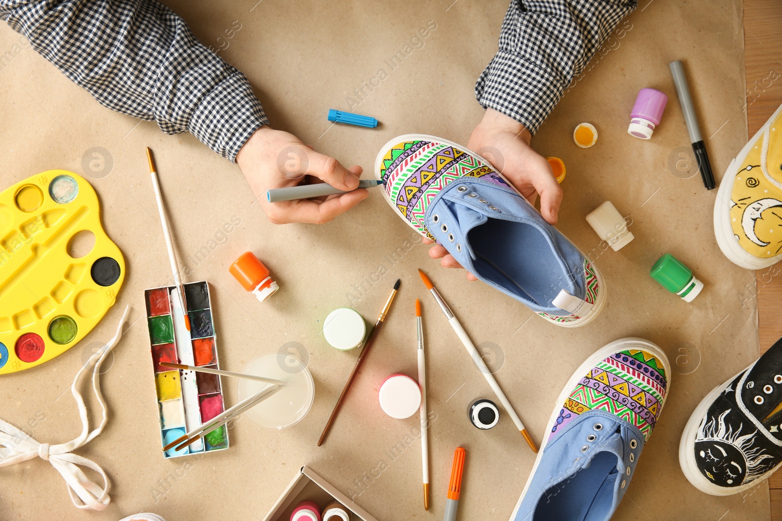 Photo of Man painting on sneaker at table, top view. Customized shoes