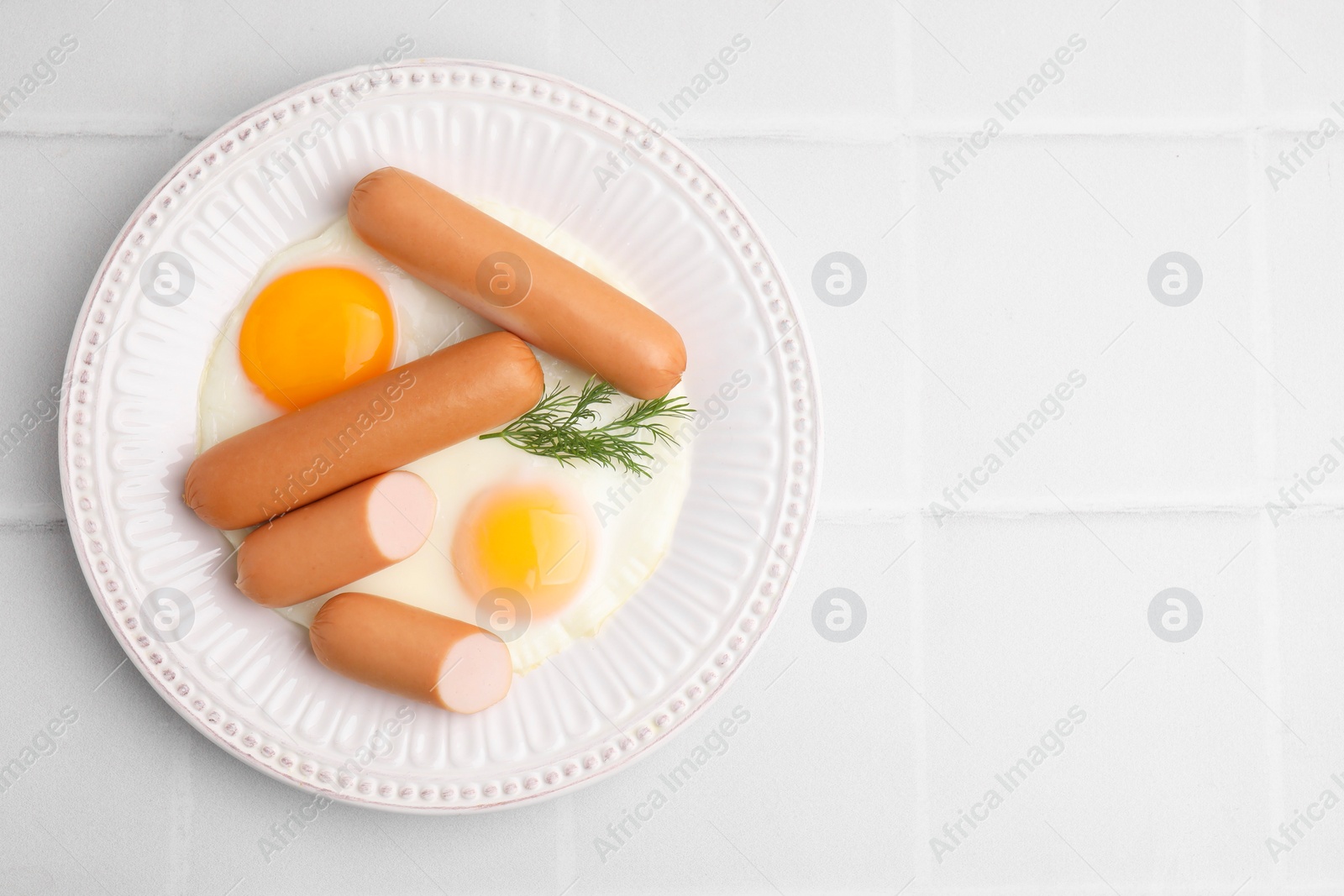 Photo of Delicious boiled sausages, fried eggs and dill on white tiled table, top view. Space for text