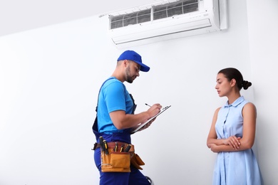 Photo of Professional technician speaking with woman about air conditioner indoors