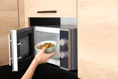 Photo of Young woman using microwave oven in kitchen