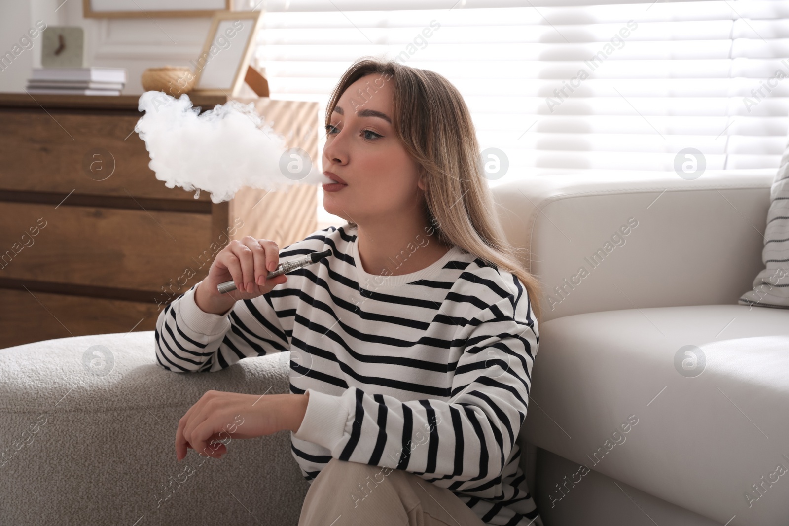 Photo of Beautiful young woman using electronic cigarette at home