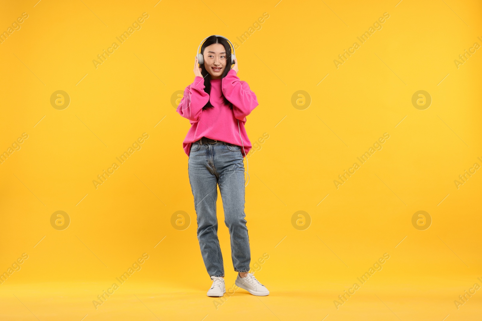 Photo of Portrait of smiling woman in headphones on orange background. Space for text