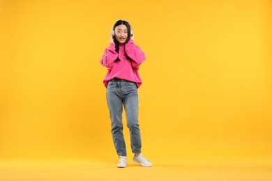 Portrait of smiling woman in headphones on orange background. Space for text