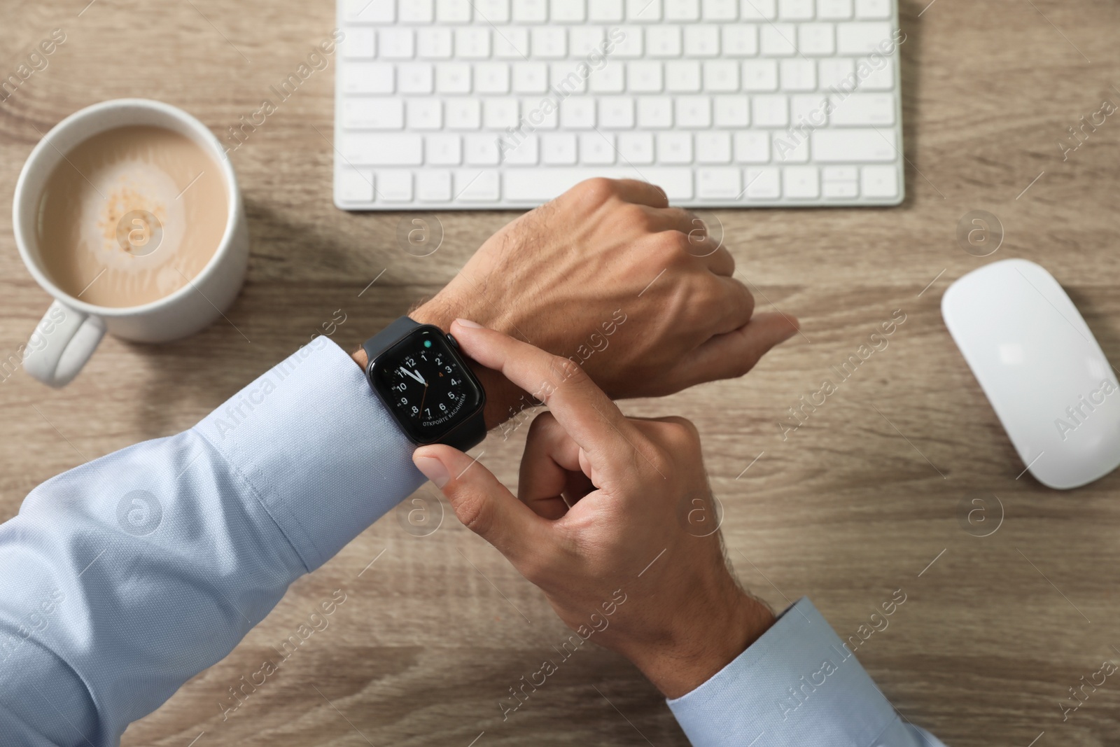 Image of MYKOLAIV, UKRAINE - OCTOBER 04, 2019: Man using Apple Watch to check time at wooden table, top view