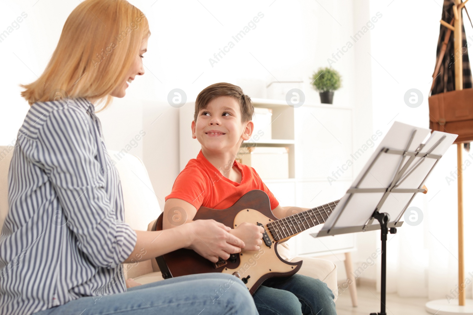 Photo of Little boy playing guitar with his teacher at music lesson. Learning notes