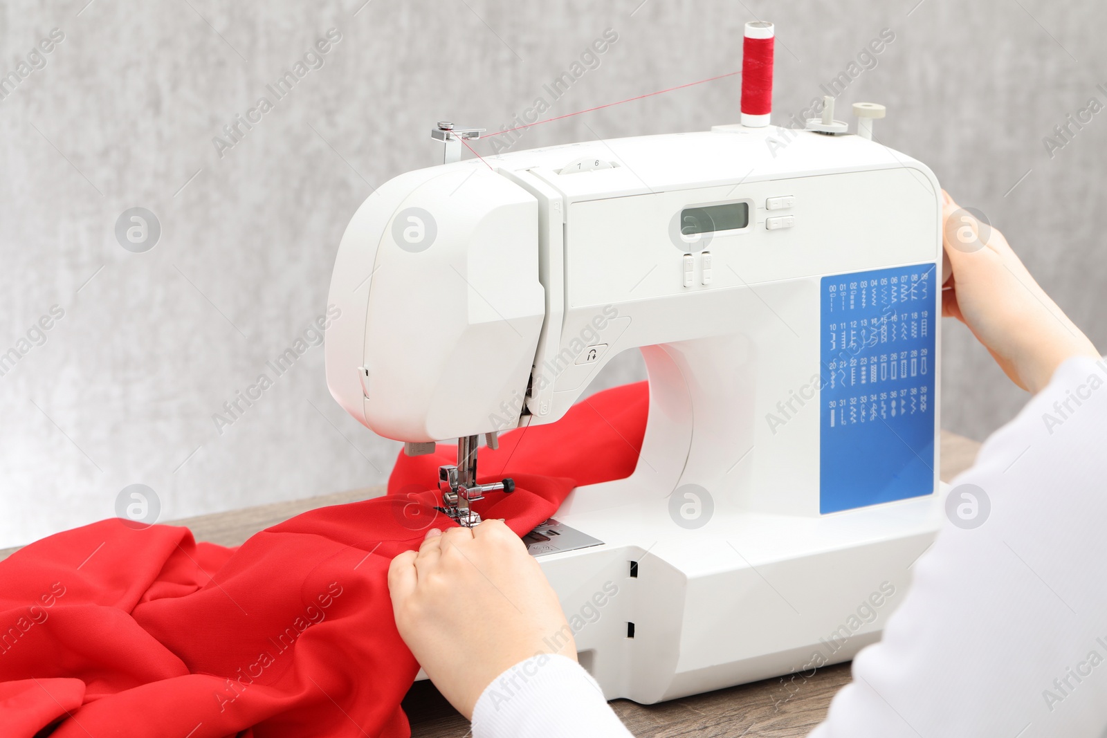 Photo of Seamstress working with sewing machine at wooden table indoors, closeup