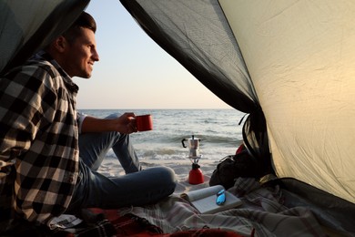 Photo of Man with cup of hot drink in camping tent