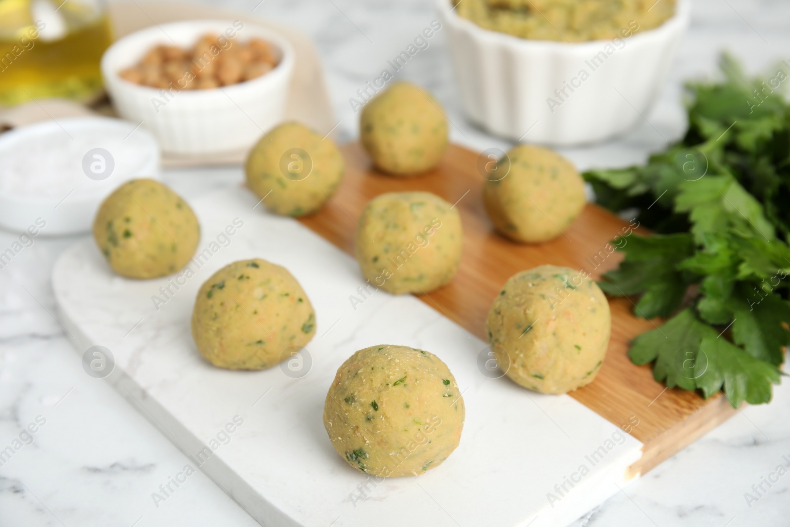 Photo of Raw falafel balls and parsley on white marble table