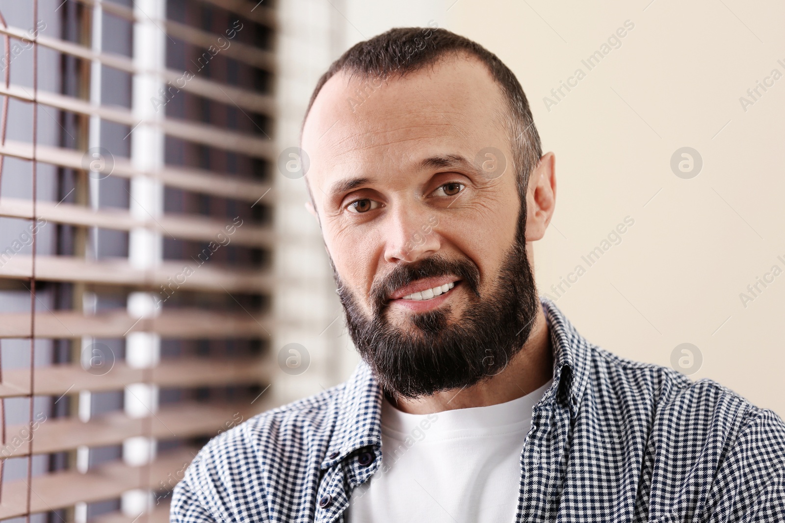 Photo of Portrait of handsome mature man near window with blinds indoors