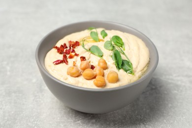 Photo of Tasty hummus with garnish in bowl on grey table