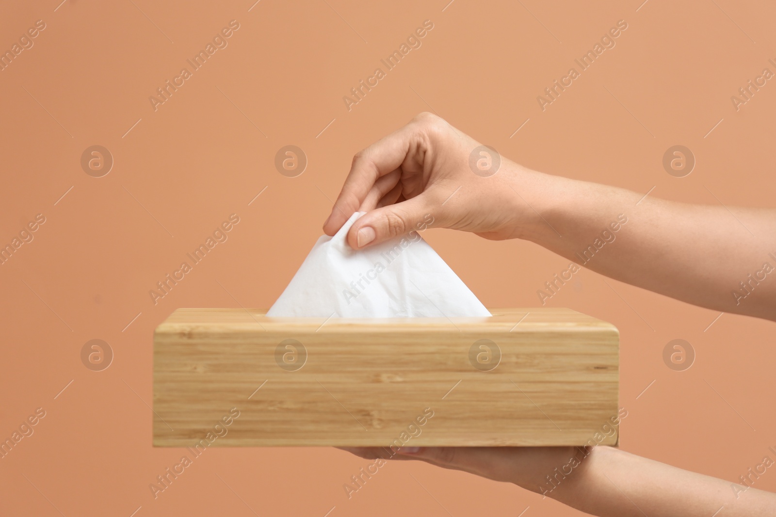 Photo of Woman taking paper tissue from holder on light brown background, closeup