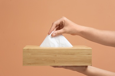 Woman taking paper tissue from holder on light brown background, closeup