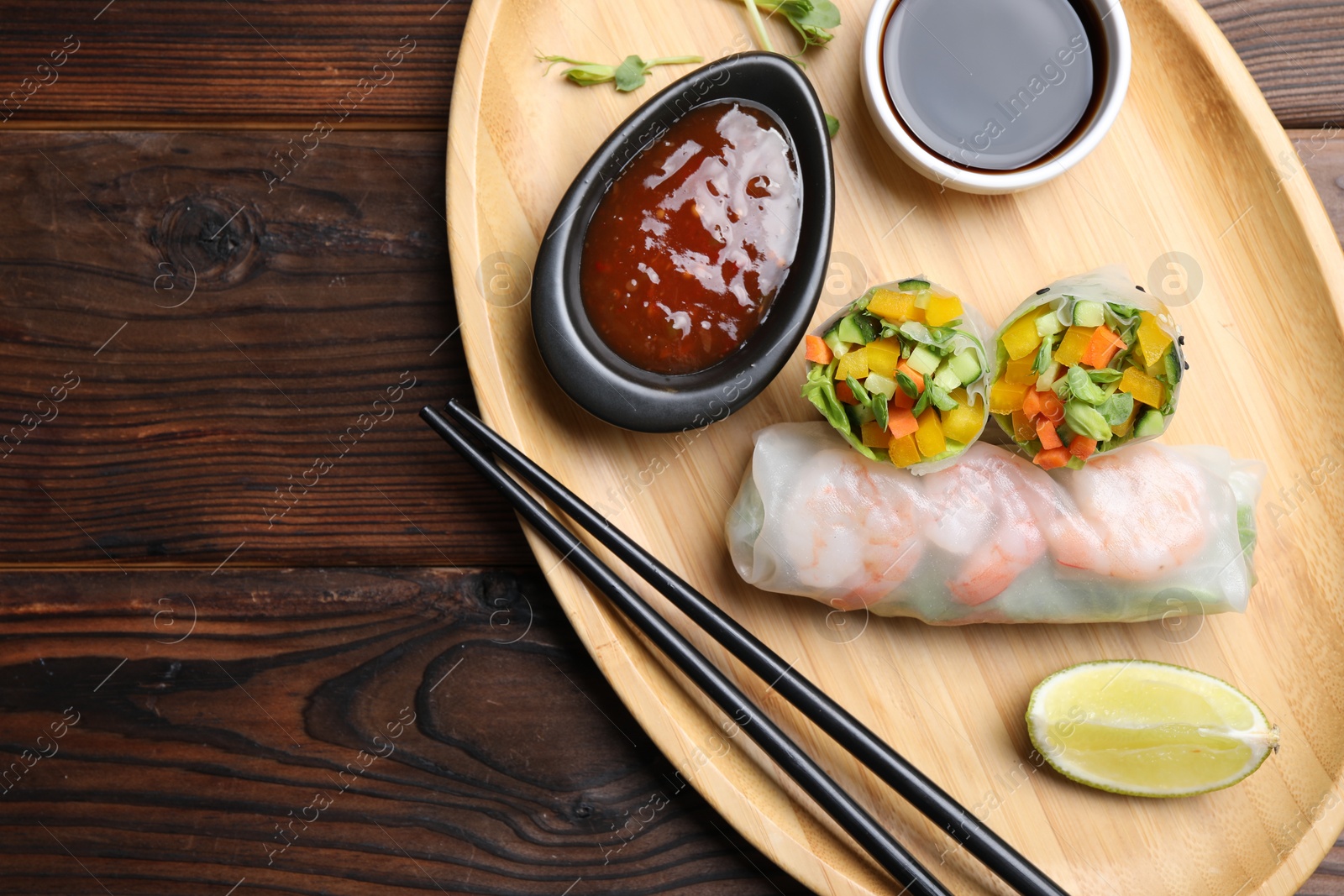 Photo of Tasty spring rolls served with sauces on wooden table, top view. Space for text