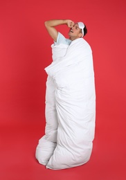 Photo of Man in sleeping mask wrapped with blanket on red background