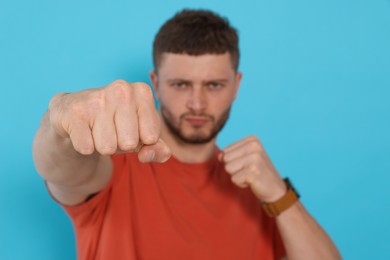 Photo of Young man ready to fight against light blue background, focus on hand. Space for text