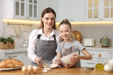 Photo of Making bread. Mother and her daughter preparing dough at wooden table in kitchen