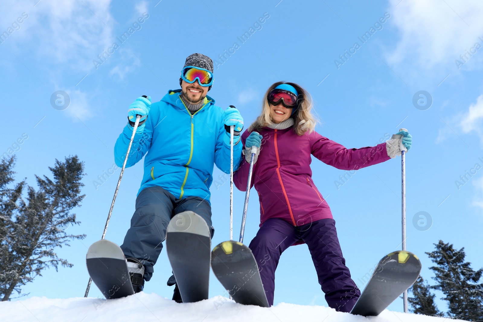 Photo of Happy couple with ski equipment outdoors, view from below. Winter vacation