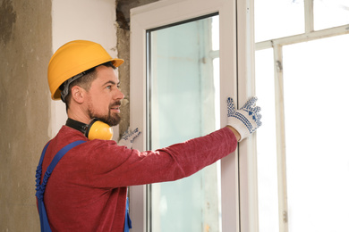 Photo of Worker in uniform installing plastic window indoors