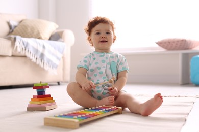 Cute little child playing with xylophone on floor at home