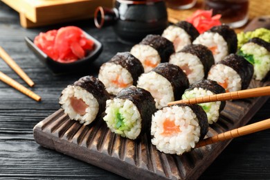 Photo of Set of delicious sushi rolls and chopsticks on black wooden table, closeup