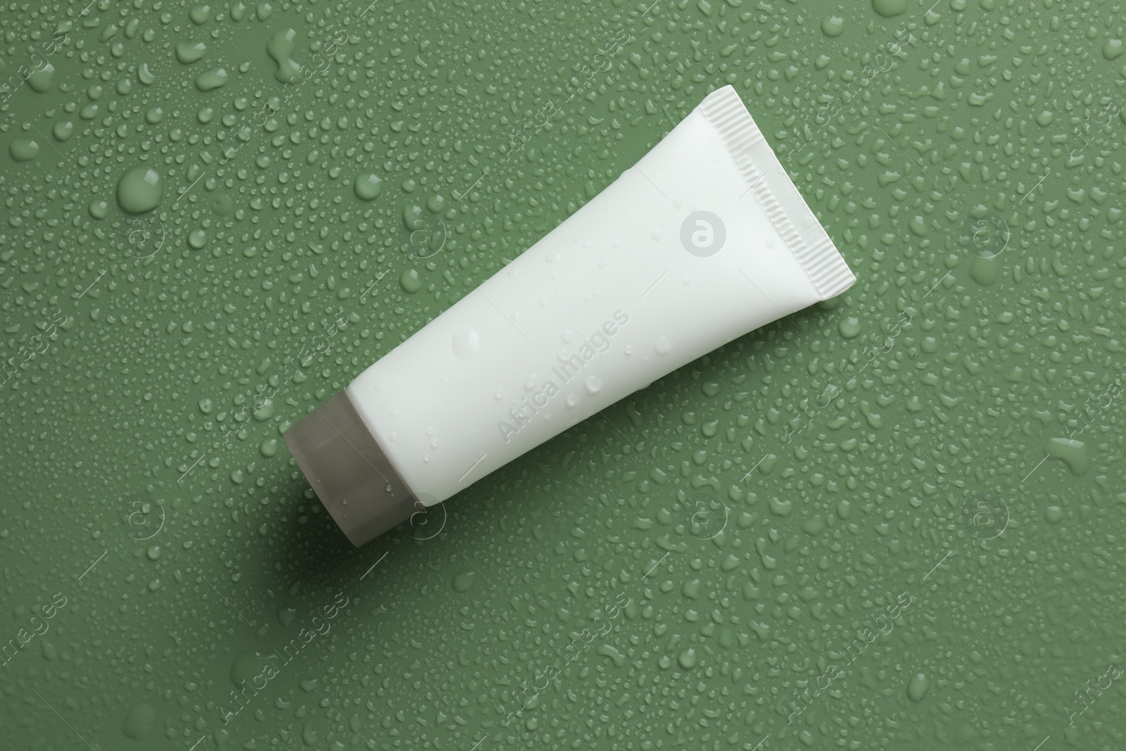 Photo of Moisturizing cream in tube on green background with water drops, top view