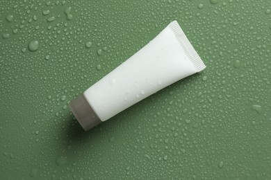 Moisturizing cream in tube on green background with water drops, top view