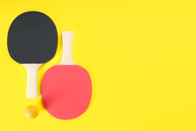 Ping pong rackets and ball on yellow background, flat lay. Space for text