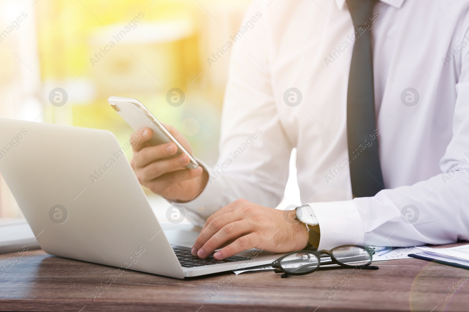 Image of Man with smartphone working with laptop at table in office, closeup