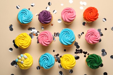 Delicious cupcakes with bright cream and confetti on beige background, flat lay