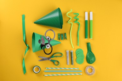 Photo of Handmade party hats, straws and tools on yellow background, flat lay
