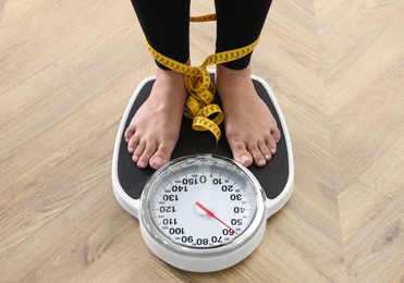 Woman tied with measuring tape using scale on floor, closeup. Overweight problem after New Year party