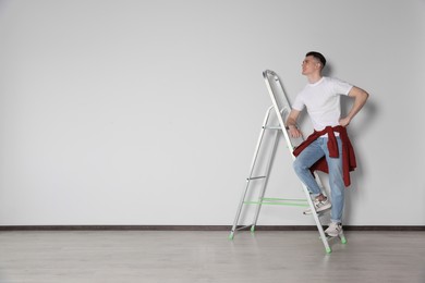 Photo of Handyman climbing up stepladder near white wall indoors. Space for text