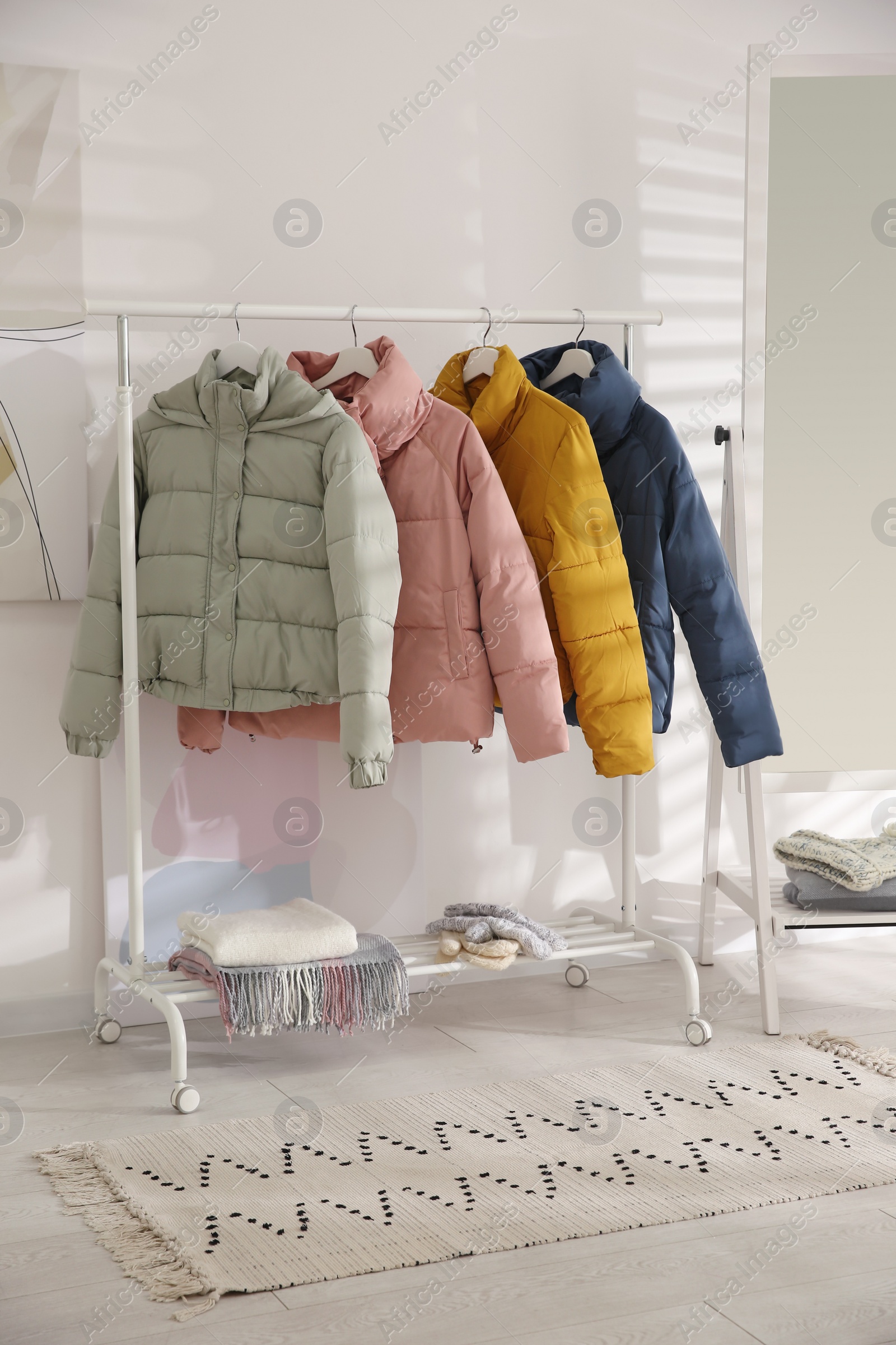 Photo of Different warm jackets on rack in stylish room interior