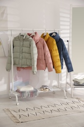 Different warm jackets on rack in stylish room interior