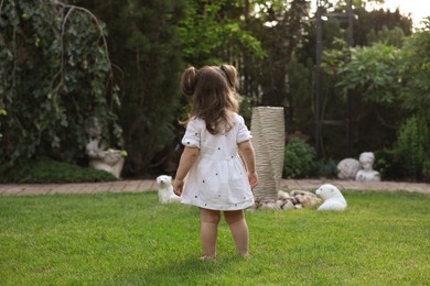 Cute little girl walking on green grass in park, back view
