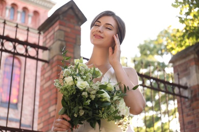 Photo of Gorgeous bride in beautiful wedding dress with bouquet near church