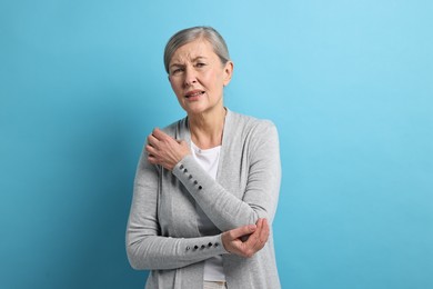 Arthritis symptoms. Woman suffering from pain in elbow on light blue background