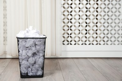 Photo of Basket with crumpled paper on floor indoors. Space for text