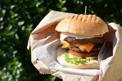 Photo of Delicious burger in paper wrap outdoors, closeup
