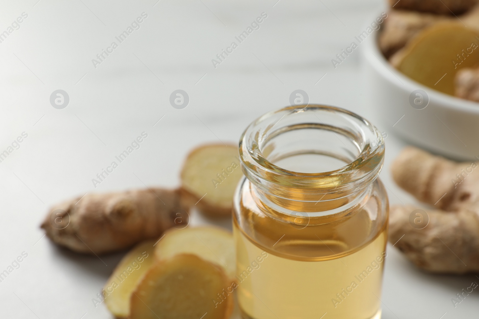 Photo of Glass bottle of ginger essential oil on white table, closeup. Space for text
