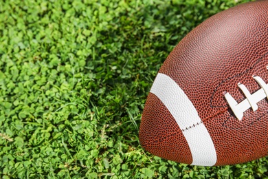 Photo of Ball for American football on fresh green field grass, closeup. Space for text