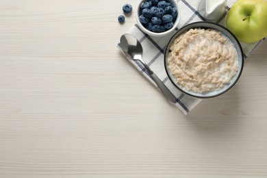 Photo of Tasty oatmeal porridge served on light wooden table, flat lay. Space for text