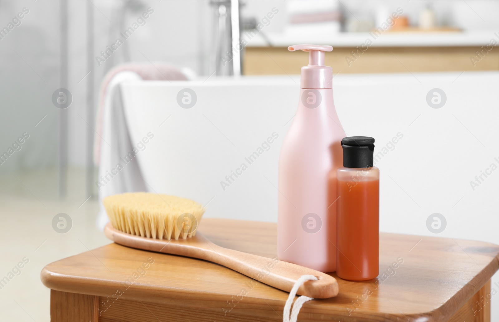 Photo of Bottles of shower gels and brush on wooden table near tub in bathroom, space for text