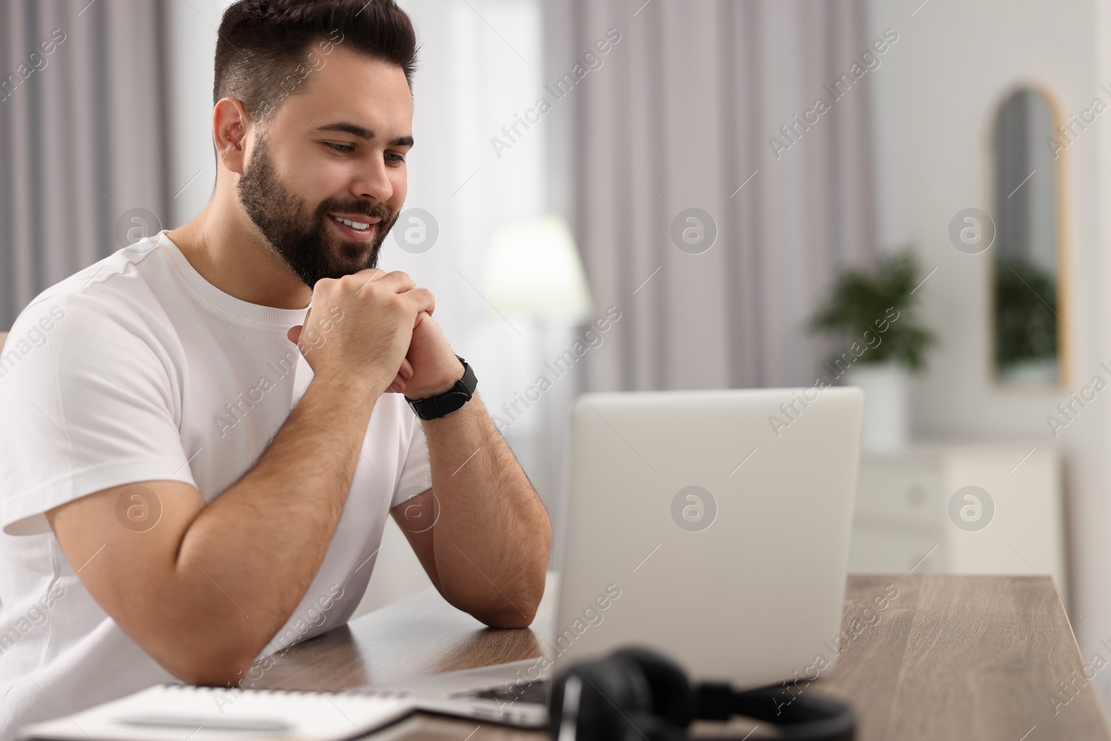 Photo of Young man watching webinar at table in room